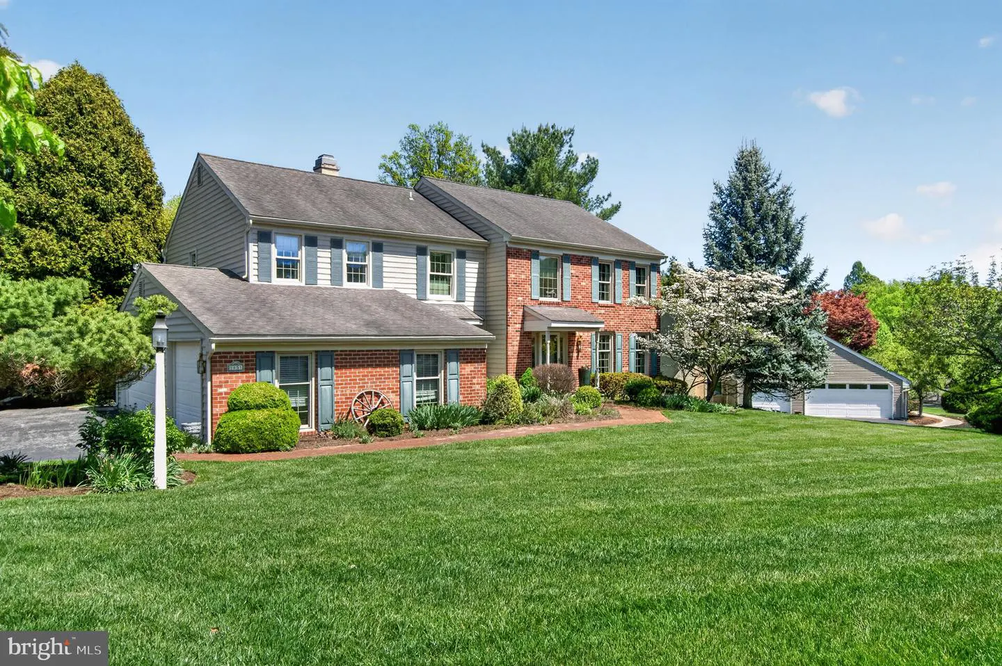 Two-story house with brick and siding, blue shutters, and a large green lawn on a sunny day.