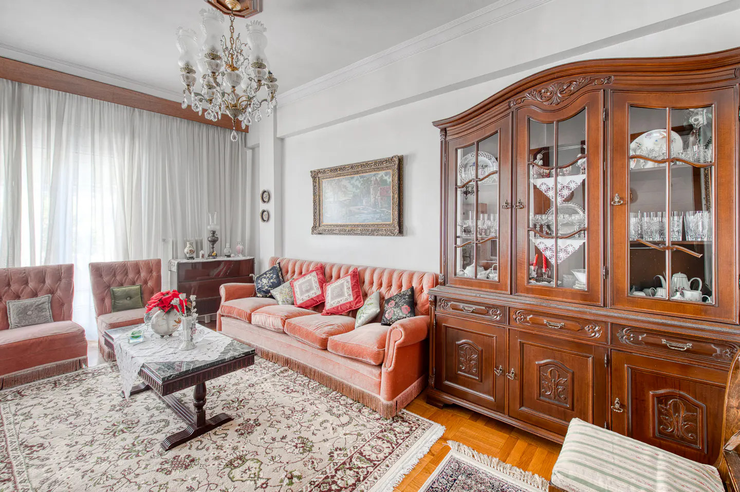 Living room with pink furniture, a patterned rug, and a dark wood china cabinet. A chandelier hangs from the ceiling.