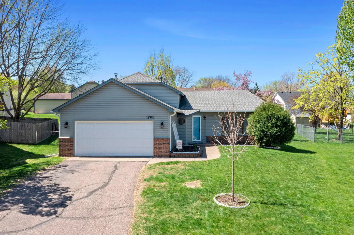 A single-family home with gray siding, a white garage door, and a green lawn under a blue sky.