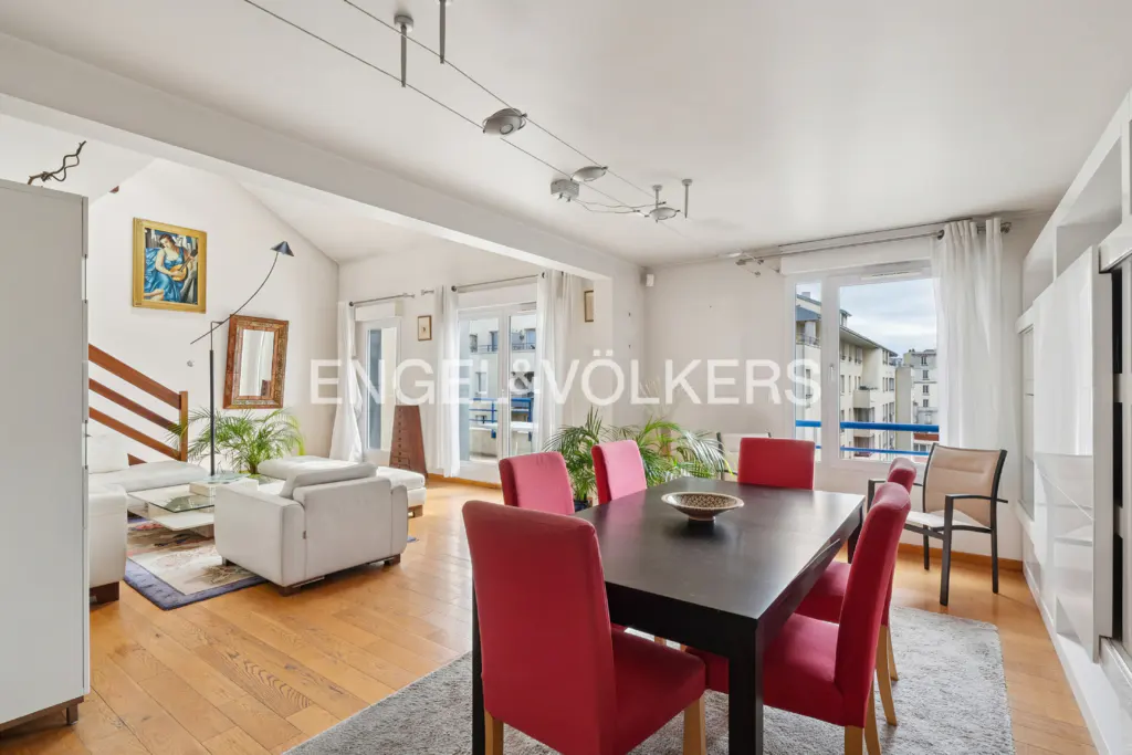 Open-concept living and dining area with hardwood floors, white walls, and red chairs around a black table. Balcony access.