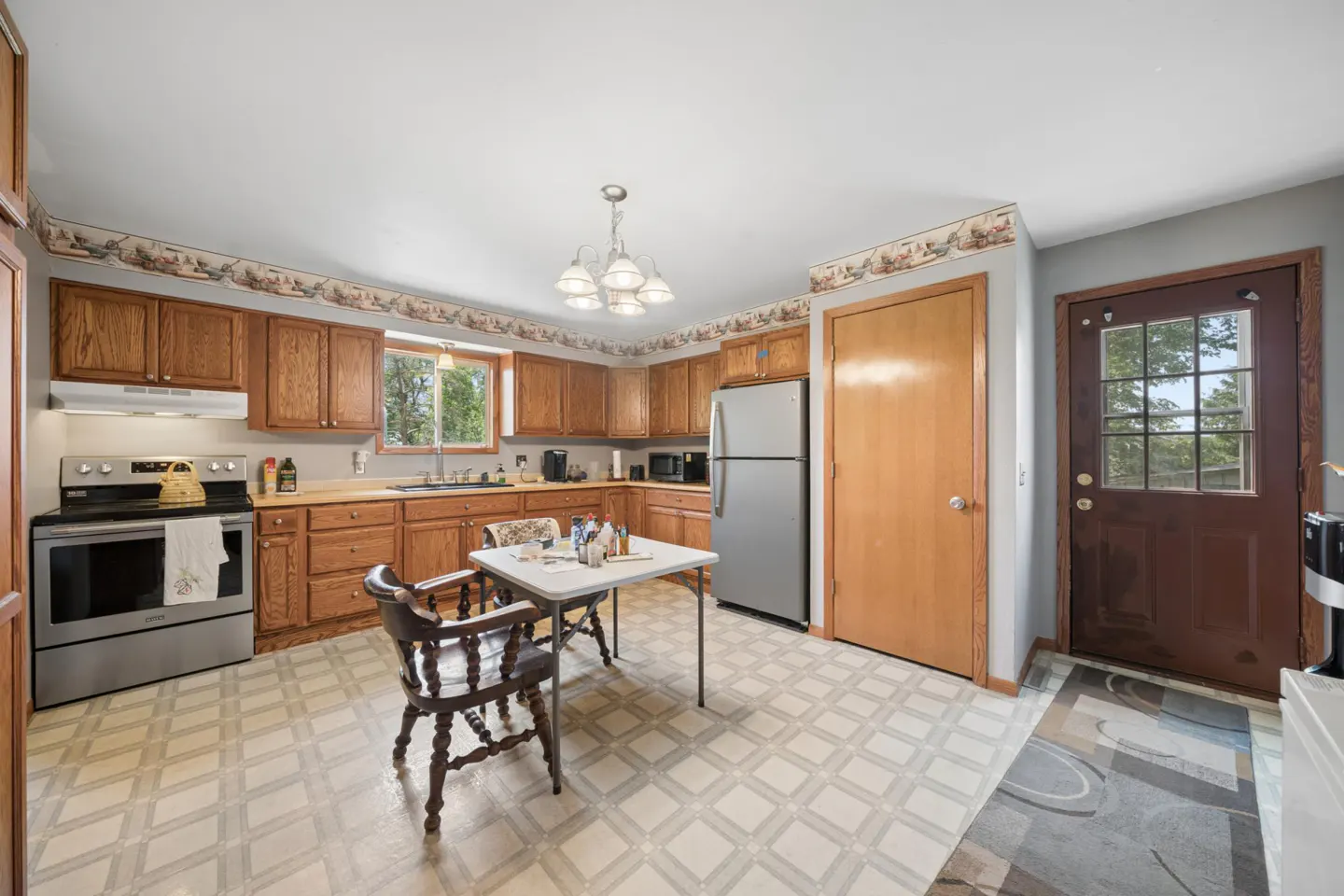 Kitchen with oak cabinets, stainless steel appliances, a small dining table, and a brown exterior door on a tiled floor.