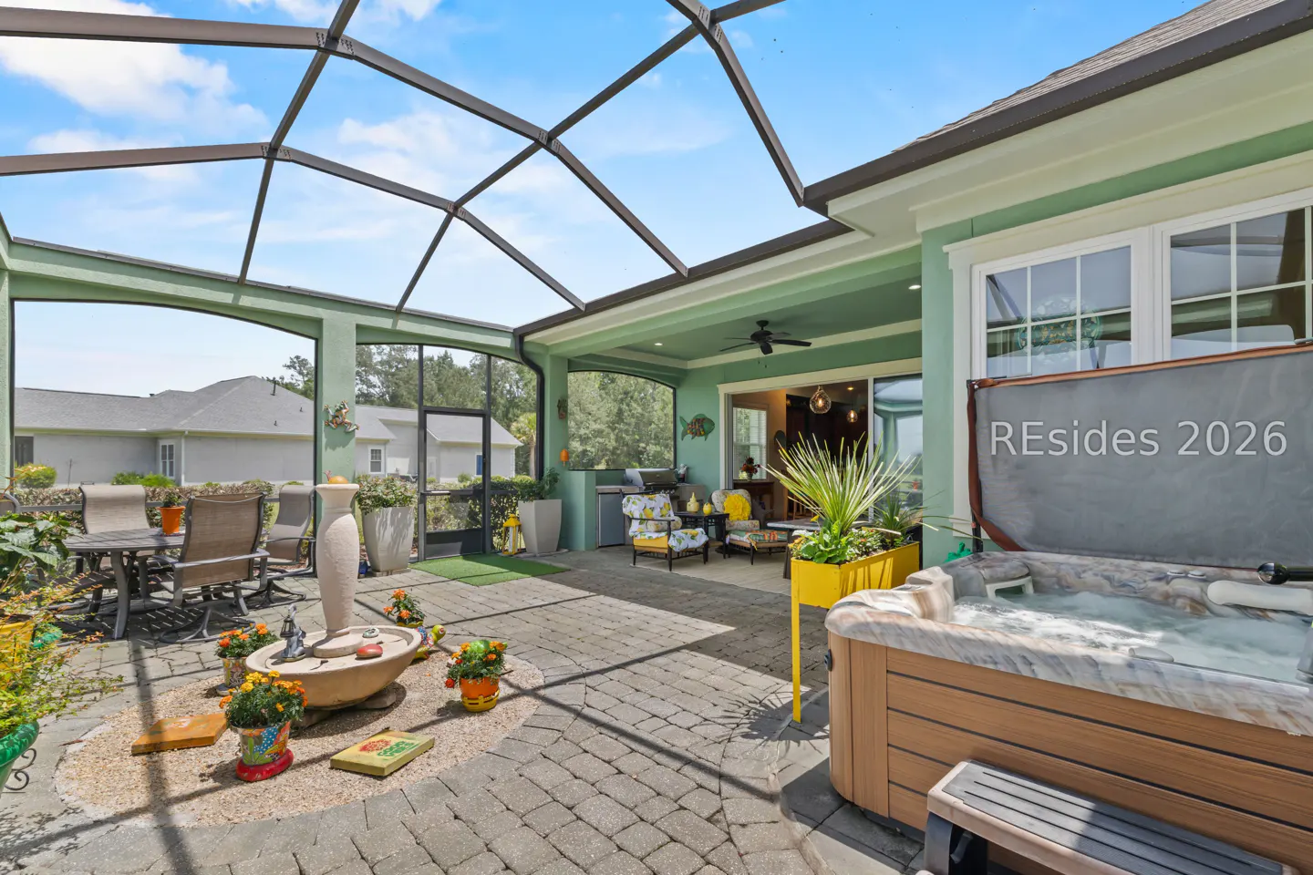Screened-in patio with a hot tub, outdoor seating, and a water feature. The patio is paved with gray bricks.