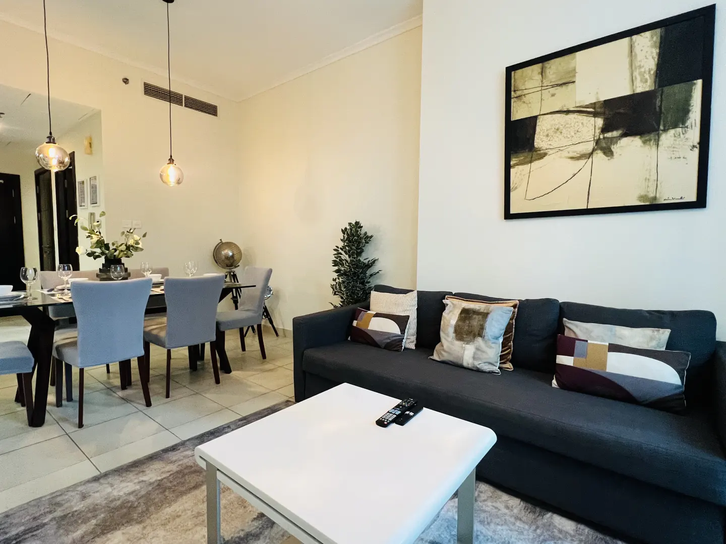 Living room with a gray sofa, white coffee table, and dining table with gray chairs. Abstract art hangs on the wall.