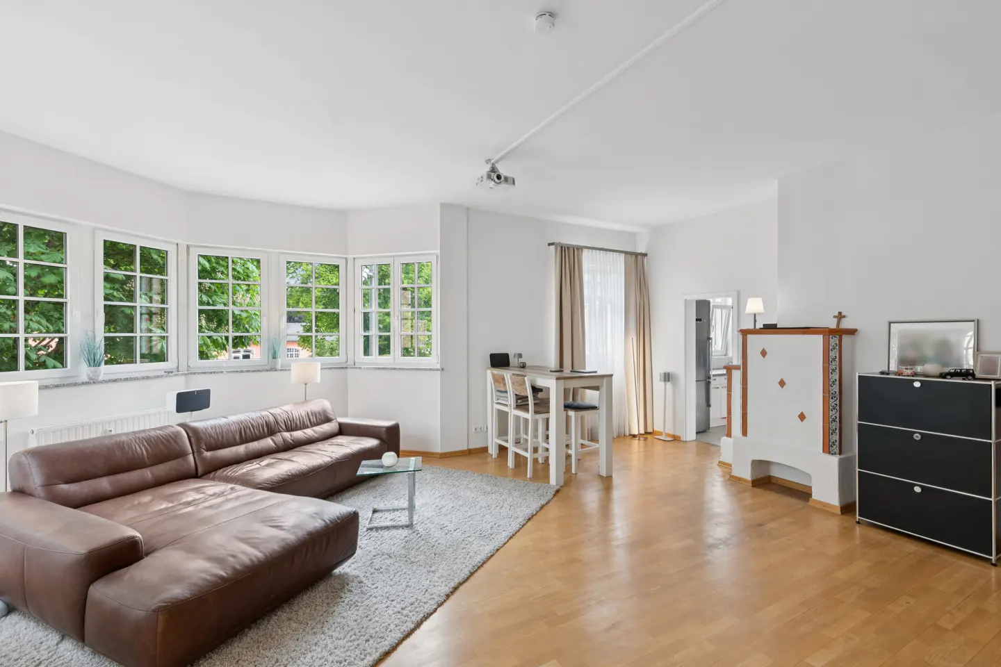 Bright living room with a brown leather sectional, gray rug, dining area, and a white tiled fireplace on hardwood floors.