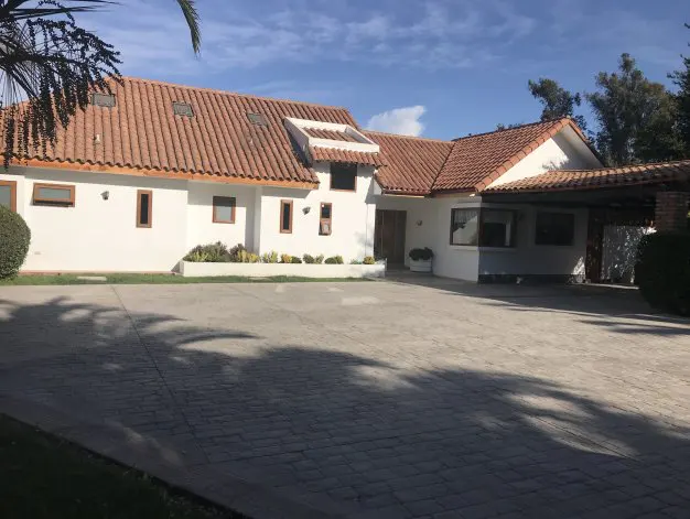 A single-story white house with a red tile roof and a large paved driveway.