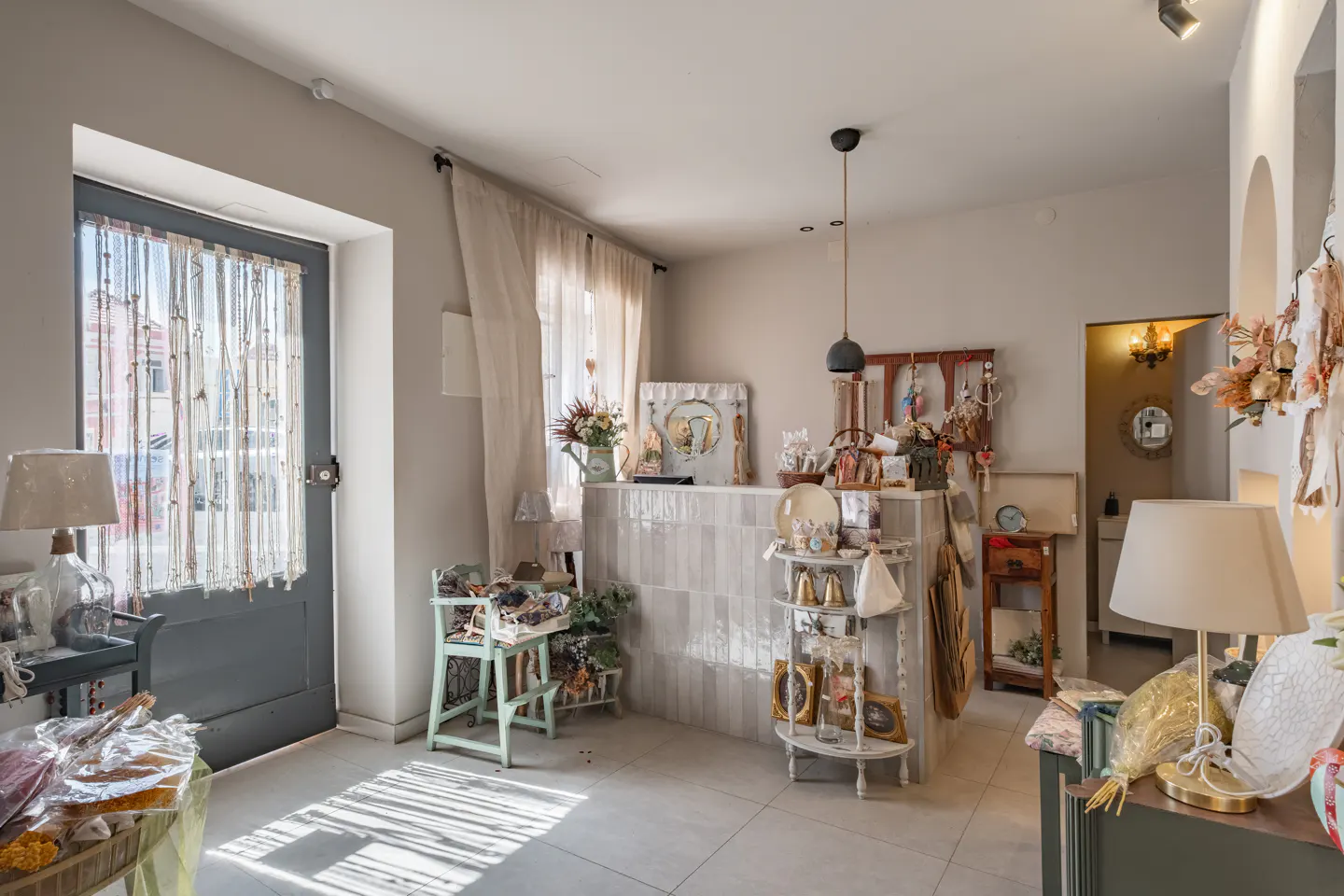 Interior view of a boutique shop with a gray door, white walls, and a tiled counter displaying various decorative items.