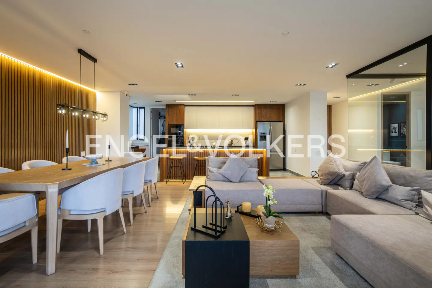 Open-concept living space with a dining table, kitchen with bar stools, and a large gray sectional sofa.