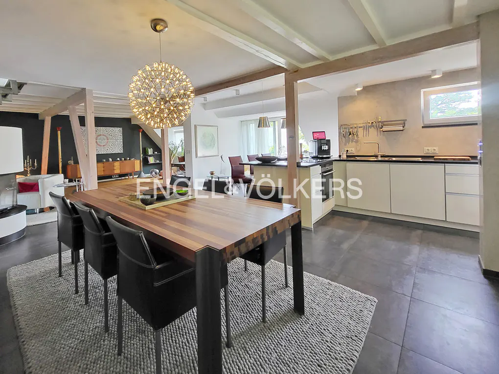 Open-concept dining and kitchen area with a wood table, black chairs, and a modern chandelier. White cabinets and gray tile flooring.