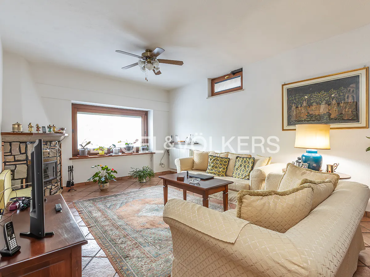Living room with white walls, tile floor, and ceiling fan. Two sofas face a wood coffee table and a large window. A stone fireplace is on the left.