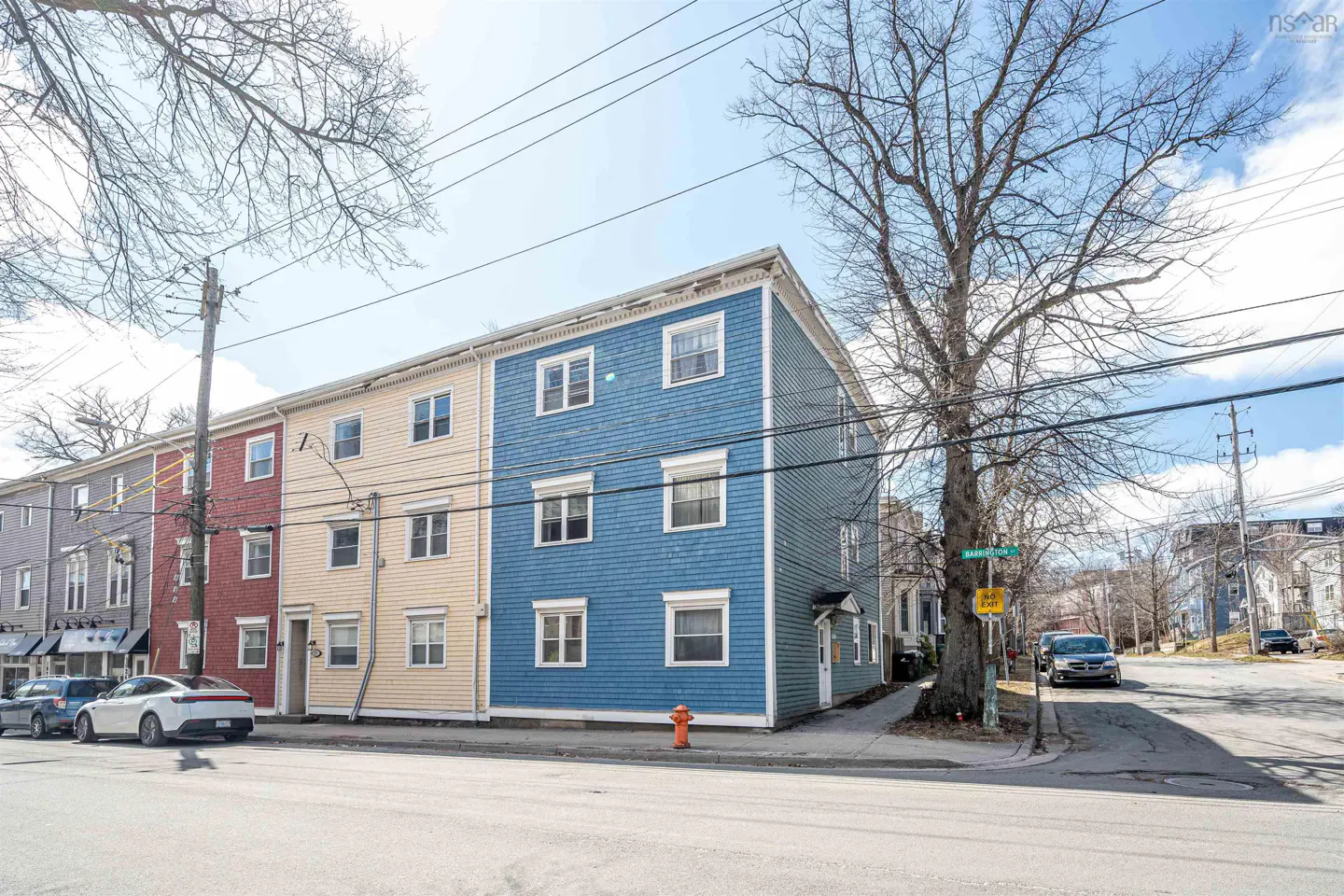 Street view of colorful three-story townhouses in gray, red, yellow, and blue with white trim and parked cars.