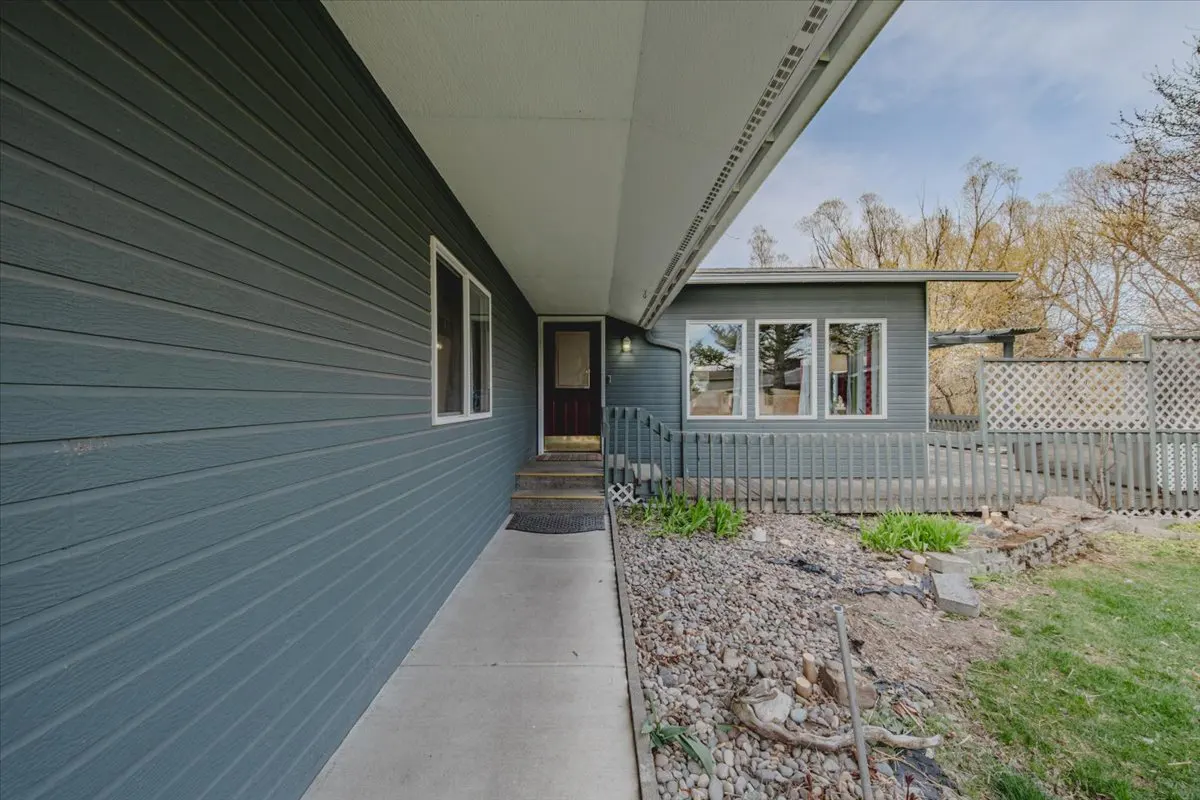 Exterior of a gray house with a brown front door, a concrete walkway, and a small deck.
