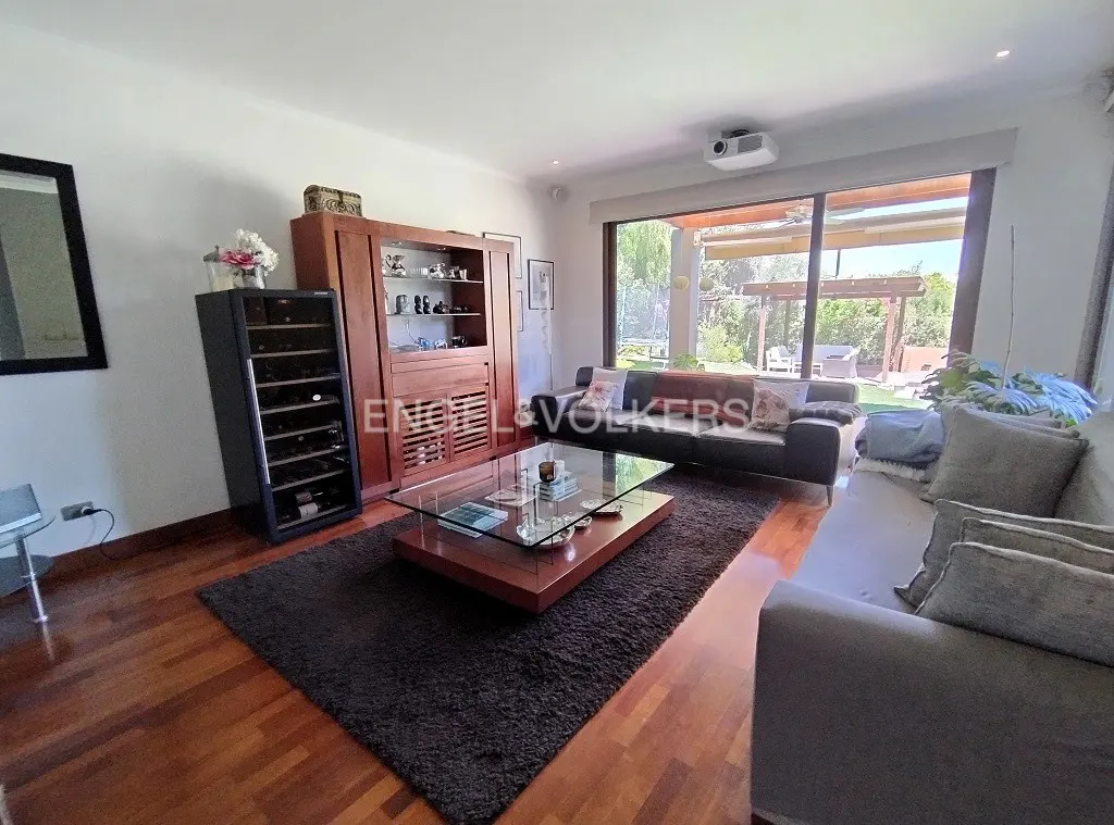 A living room with hardwood floors, a dark rug, sofas, and a glass coffee table. A large window overlooks a patio.