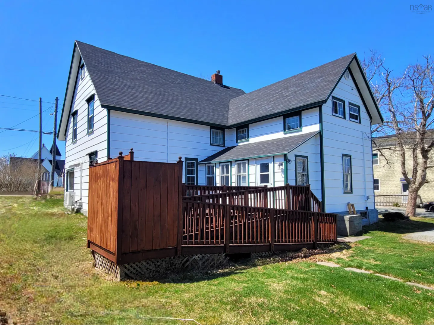 Two-story white house with a dark roof and a brown wooden deck on a sunny day.