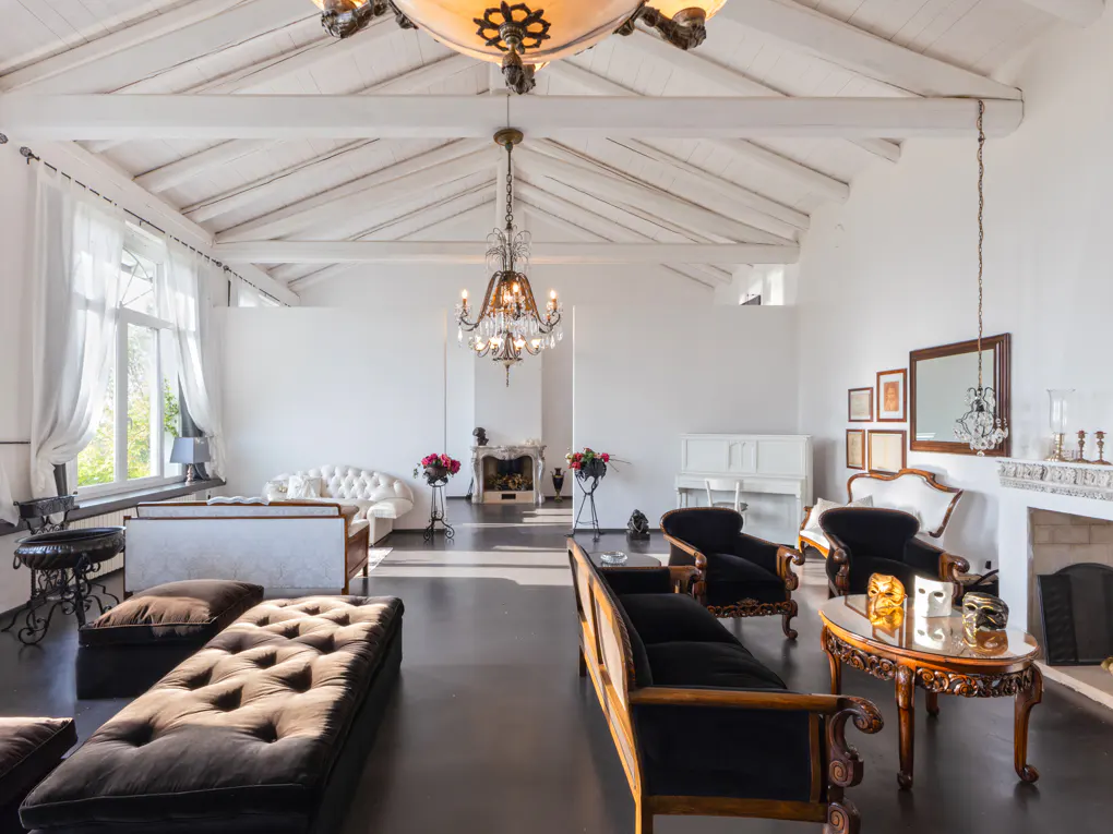 Bright, airy living room with white walls, dark wood floors, and vaulted ceiling. Chandeliers hang above sofas and a fireplace.