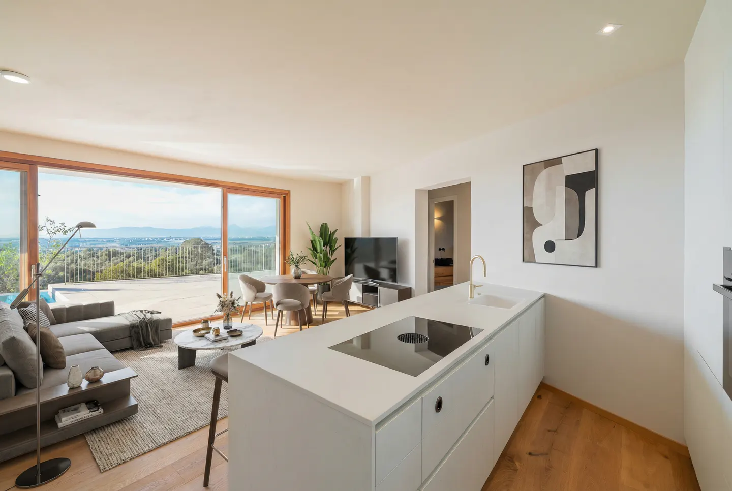 Open-concept living space with a white kitchen island, gray sofa, dining table, and a large sliding glass door to a balcony with a view.