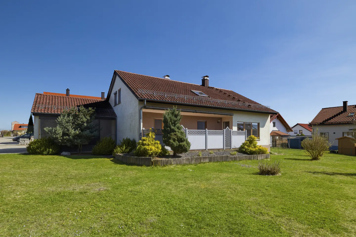 Exterior of a one-story house with a red tile roof, white walls, and a green lawn under a clear blue sky.