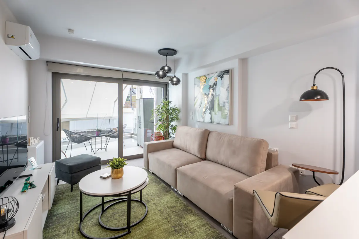 Modern living room with a beige sofa, green rug, oval coffee table, and sliding glass doors leading to a balcony.