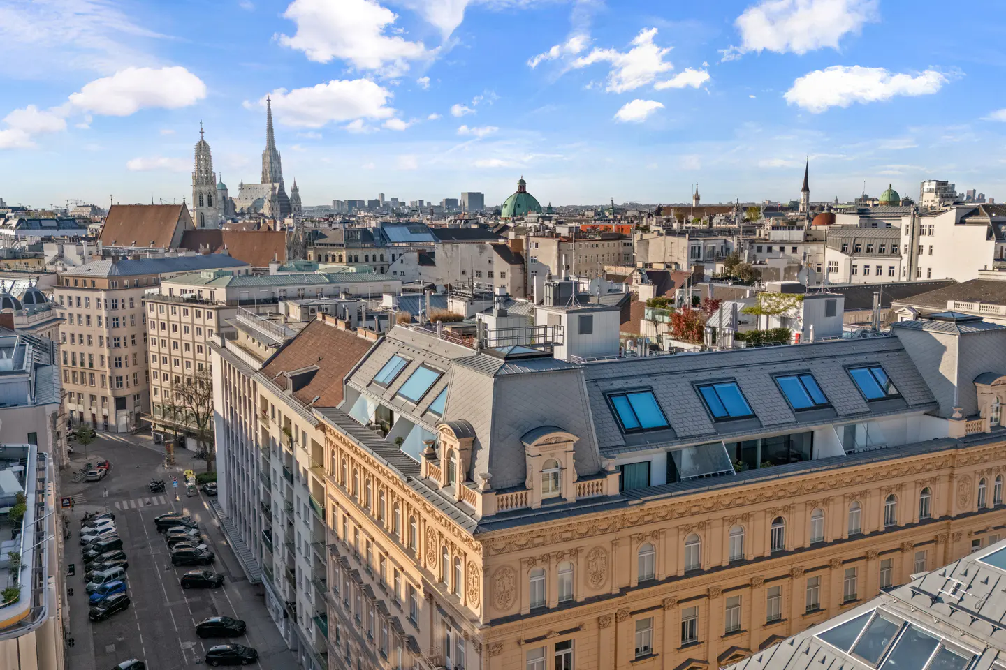 Cityscape view of Vienna, Austria, featuring historic buildings, St. Stephen's Cathedral, and a blue sky with scattered clouds.