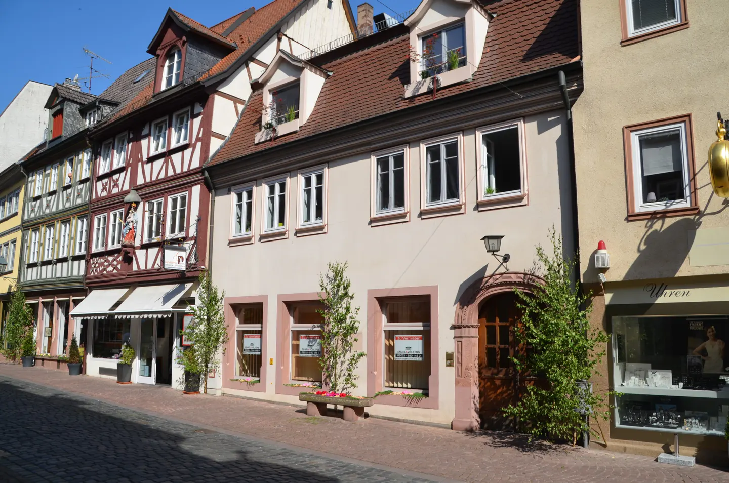 Street view of European-style buildings with red-tiled roofs and timber framing on a sunny day.