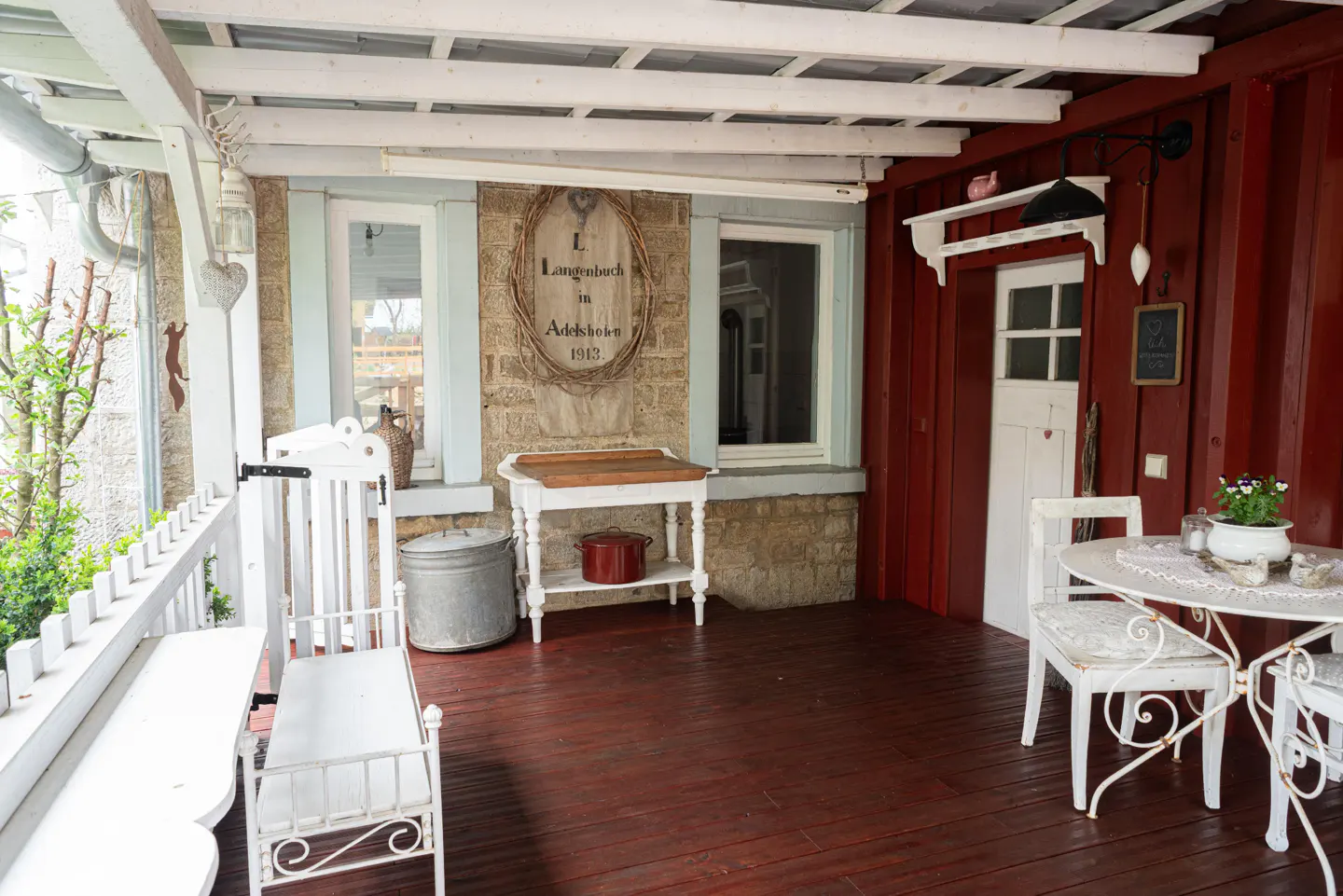 Covered porch with red wood floor, white furniture, and stone wall with sign.