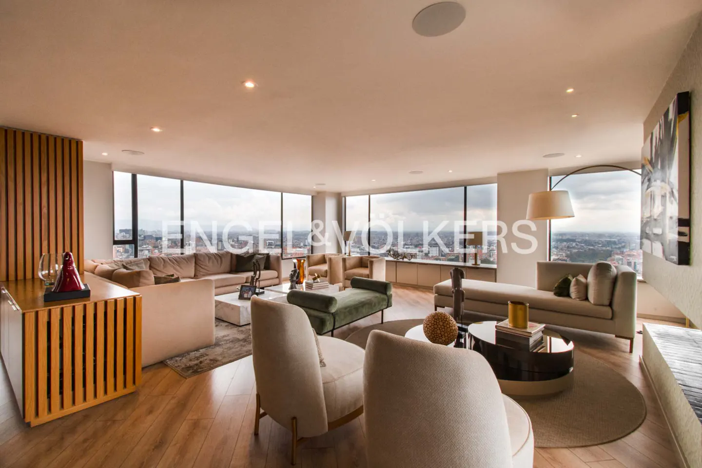 A modern living room with beige sofas, chairs, and a large window overlooking a city.