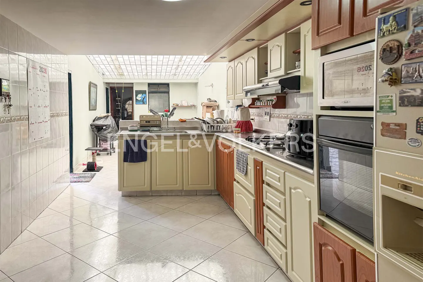 A bright kitchen with white tile floors, cream and wood cabinets, and stainless steel appliances. A glass-block ceiling provides natural light.