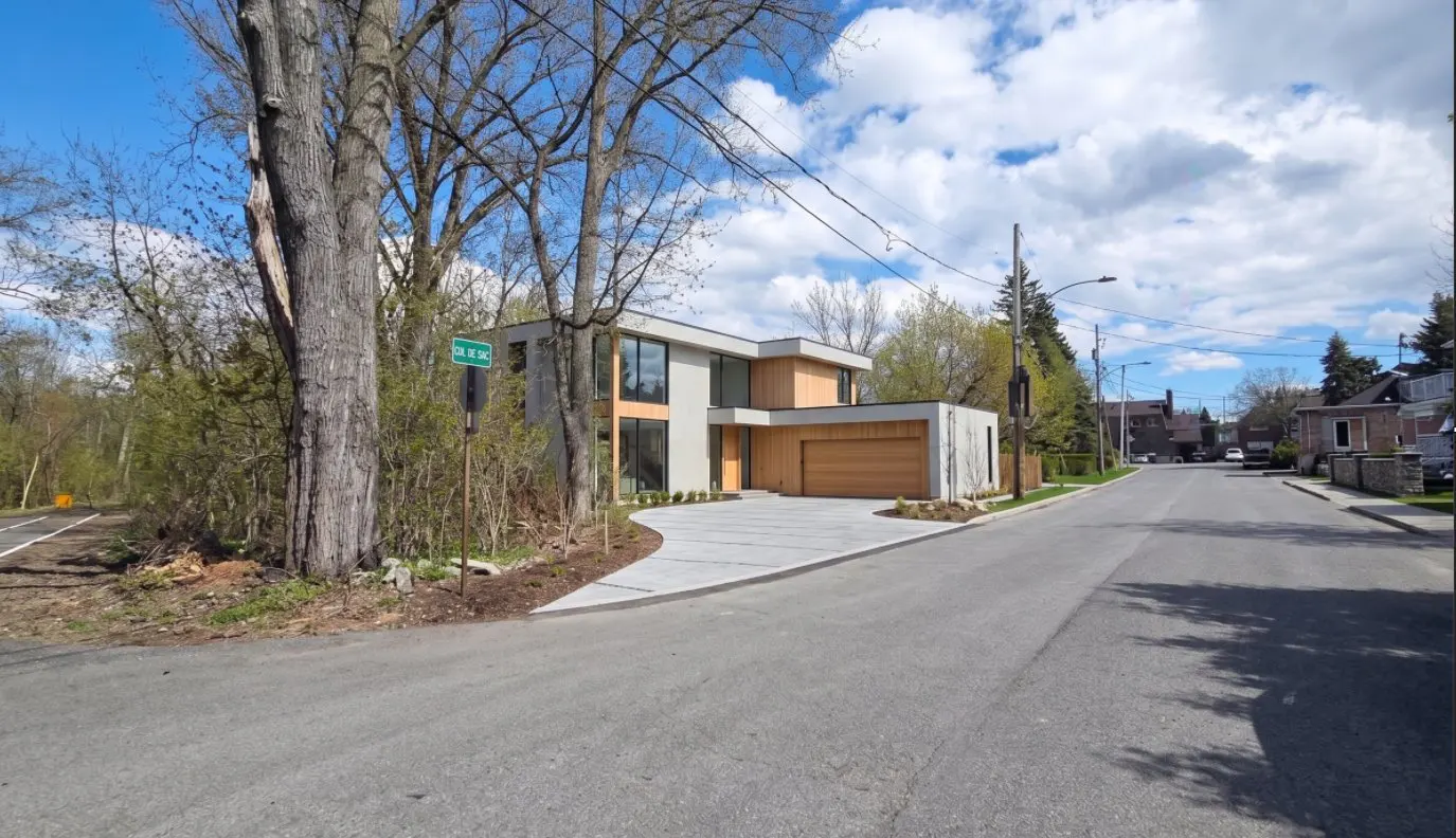 Modern two-story home with wood and concrete exterior, large windows, and a wood garage door on a tree-lined street.