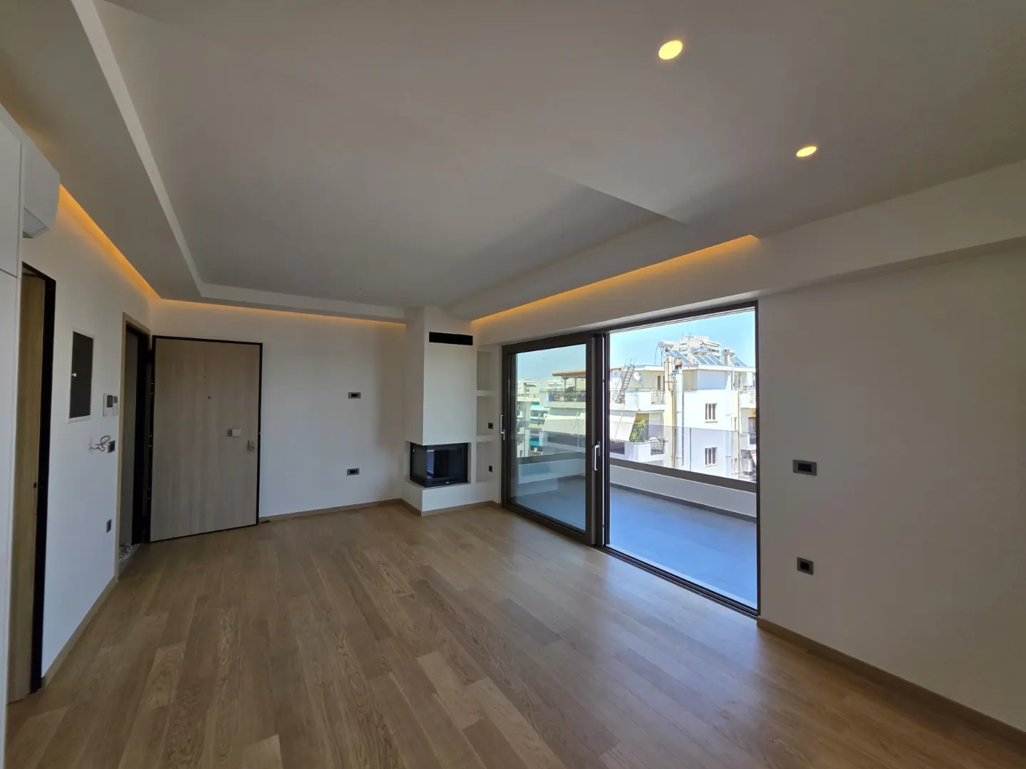 Modern living room with light wood floors, recessed ceiling lighting, a corner fireplace, and a balcony with city views.