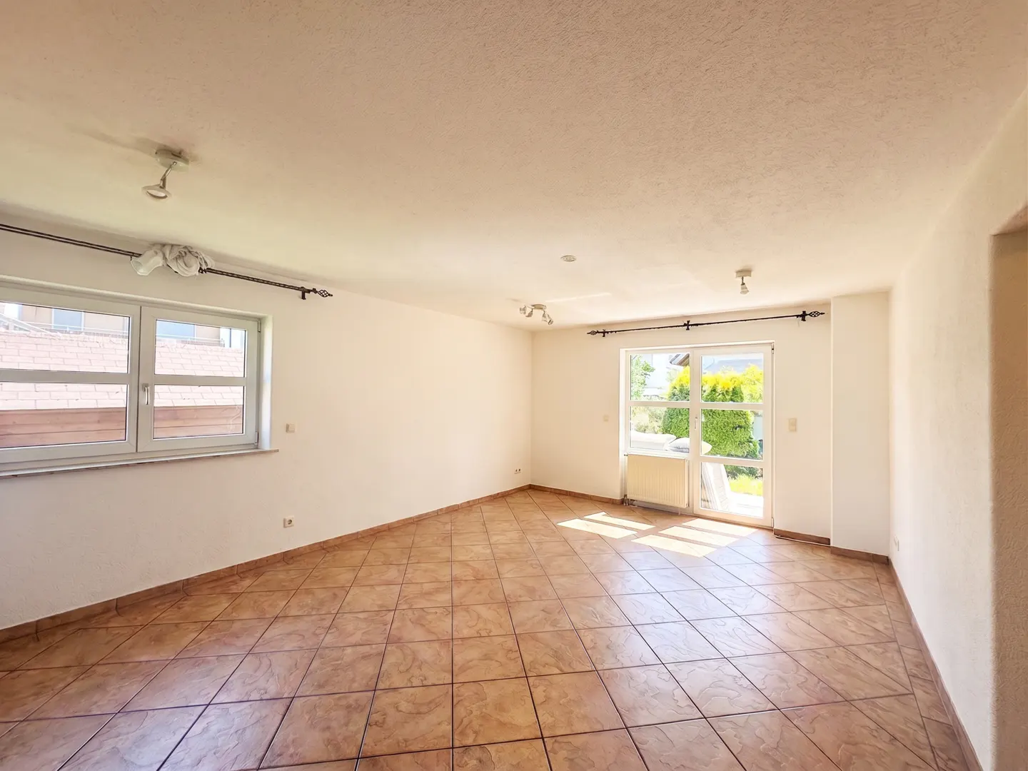 Empty room with brown tile floor, white walls, and a window and glass door to the outside.