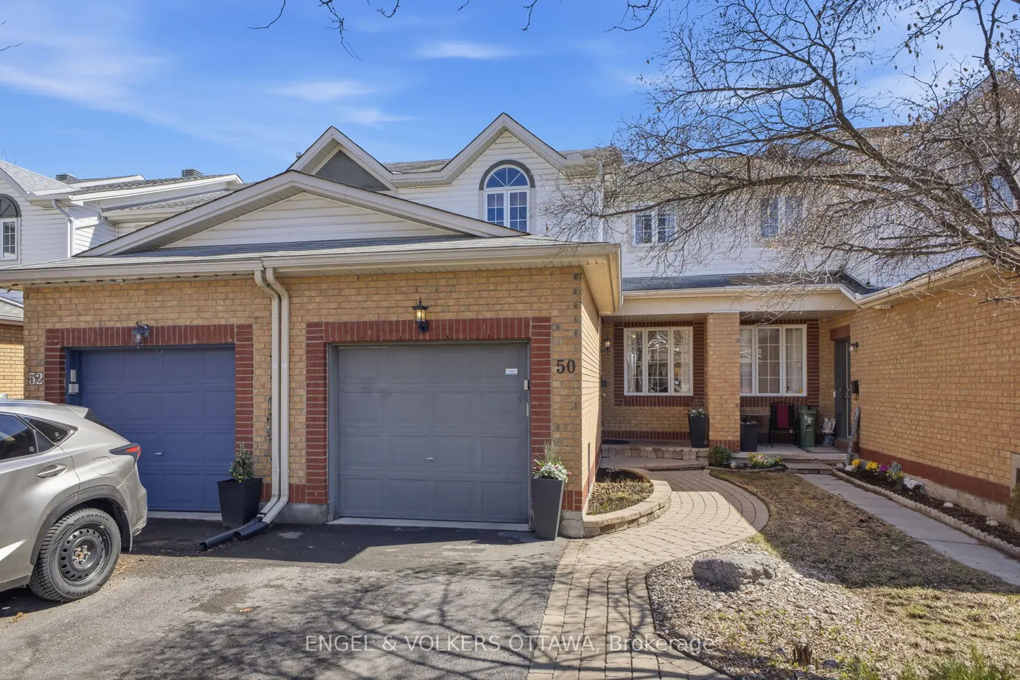 Two-story brick townhouse with gray garage doors and a curved stone walkway leading to the front door.