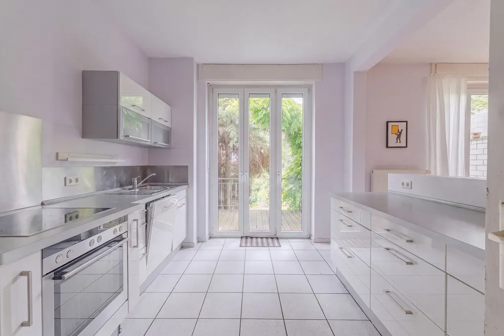 Modern galley kitchen with white cabinets, stainless steel appliances, tiled floors, and glass doors leading to a deck.