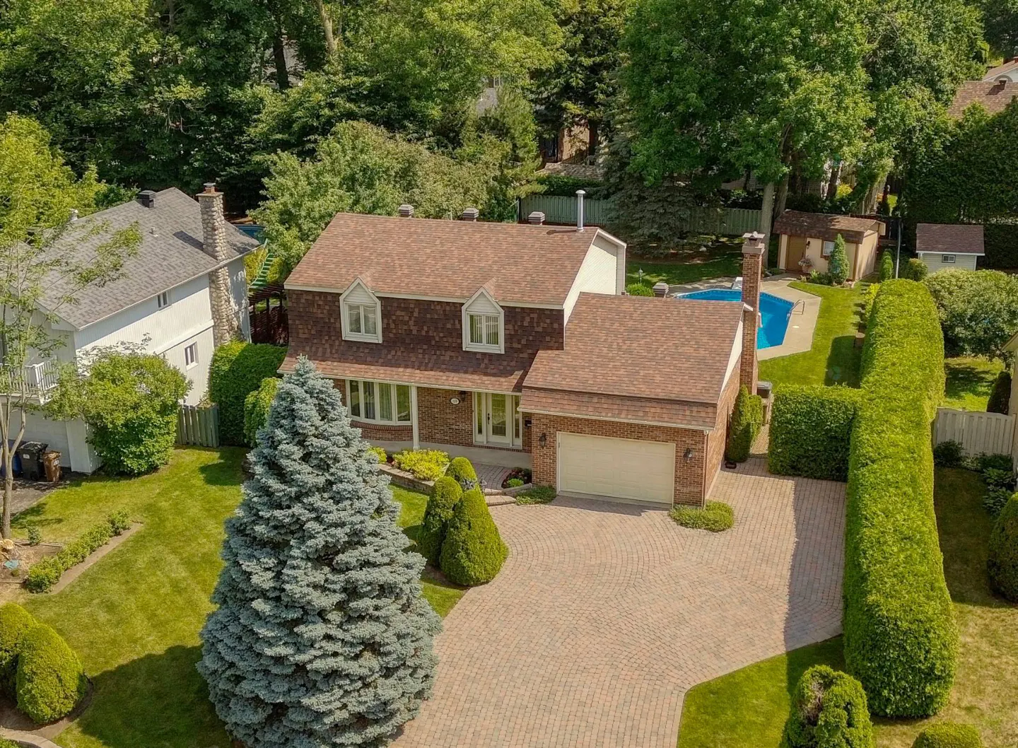 Aerial view of a brick house with a brown roof, a pool in the backyard, and a brick driveway.