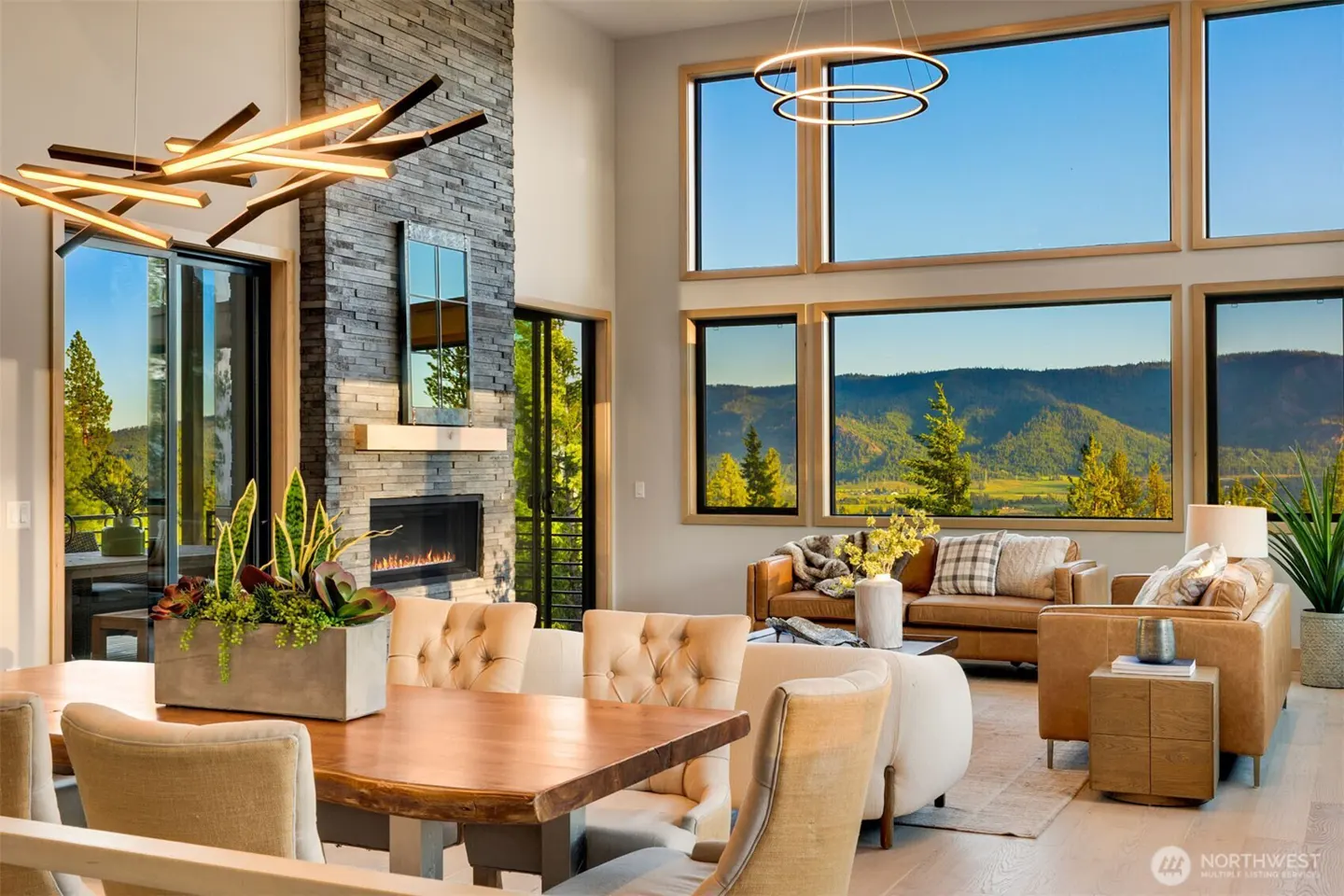 Bright, modern living room with a stone fireplace, wood table, and large windows with mountain views.