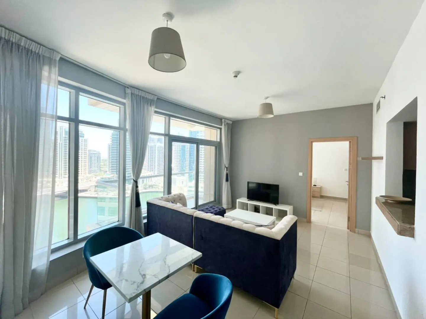 Modern living room with a blue sofa, marble dining table, and floor-to-ceiling windows overlooking a city canal view.