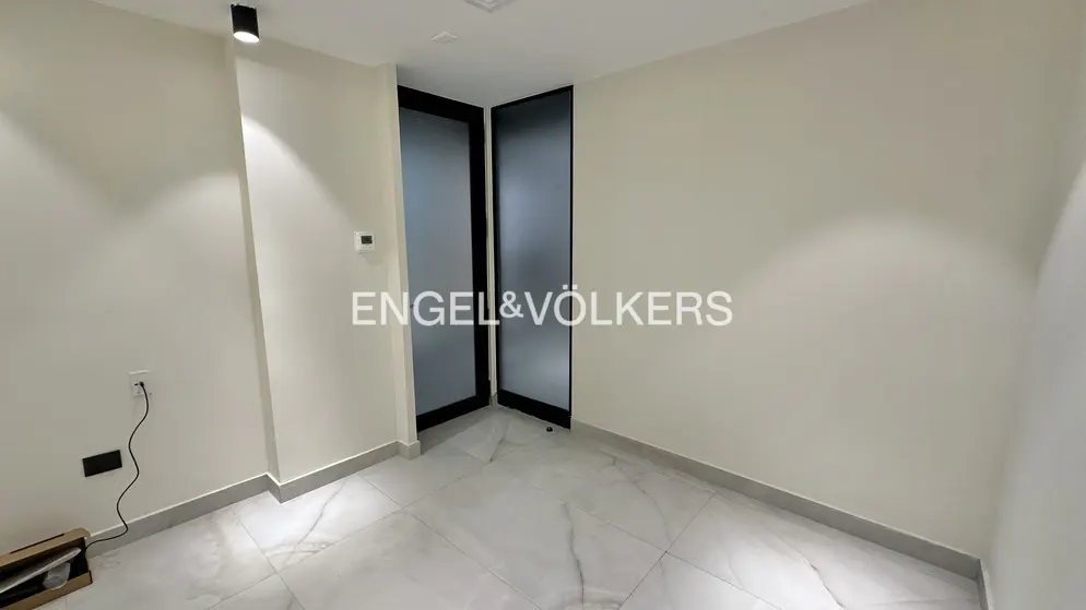 A bright, empty room with white walls and marble floors. Black framed frosted glass doors are slightly ajar. Engel & Völkers logo is superimposed.