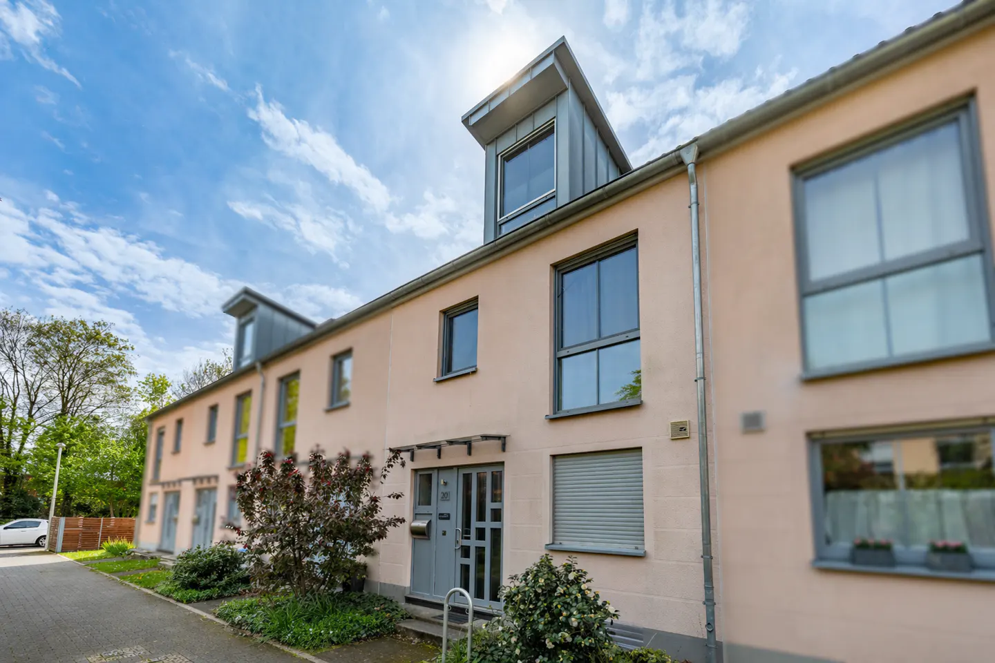 Exterior view of peach-colored townhouses with gray trim, windows, and doors under a blue sky.