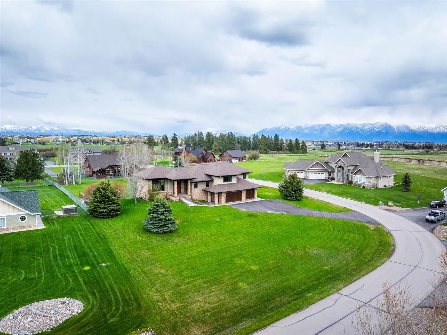 Aerial view of a tan house with a green lawn, other houses, trees, and mountains in the background.