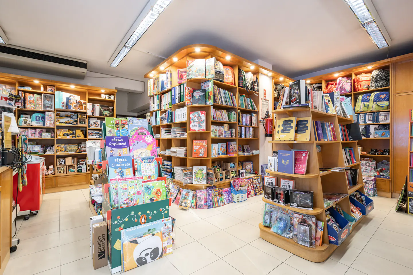 Interior view of a brightly lit bookstore with wooden shelves stocked with books, toys, and backpacks.