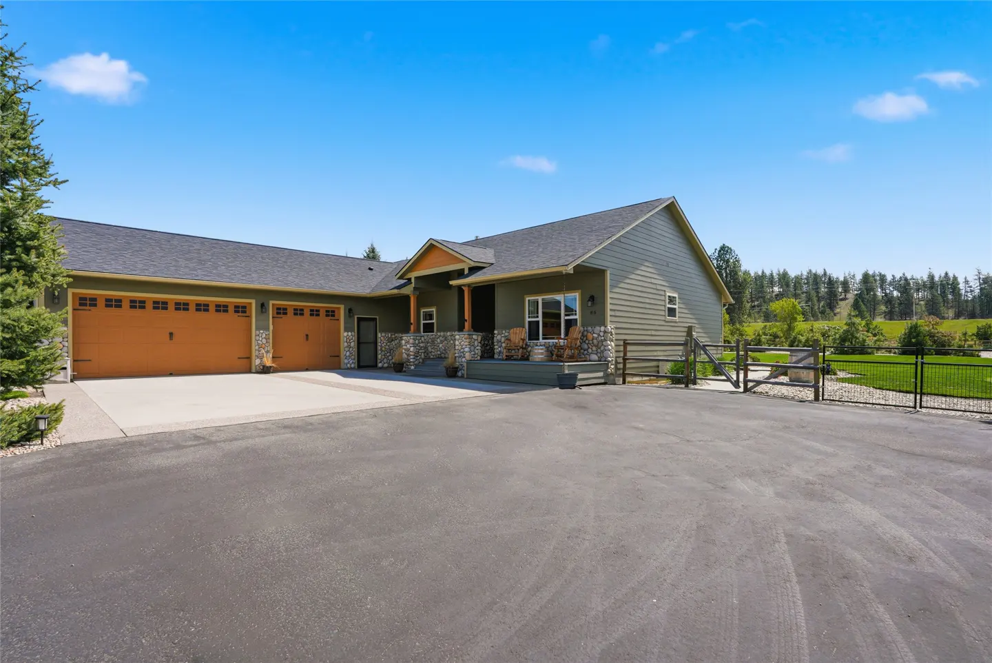 A single-story olive green house with a gray roof, brown garage doors, and a stone porch under a blue sky.
