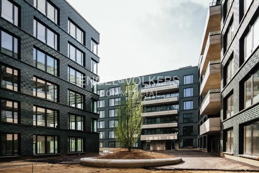 Exterior view of modern, dark brick apartment buildings surrounding a central courtyard with a tree.