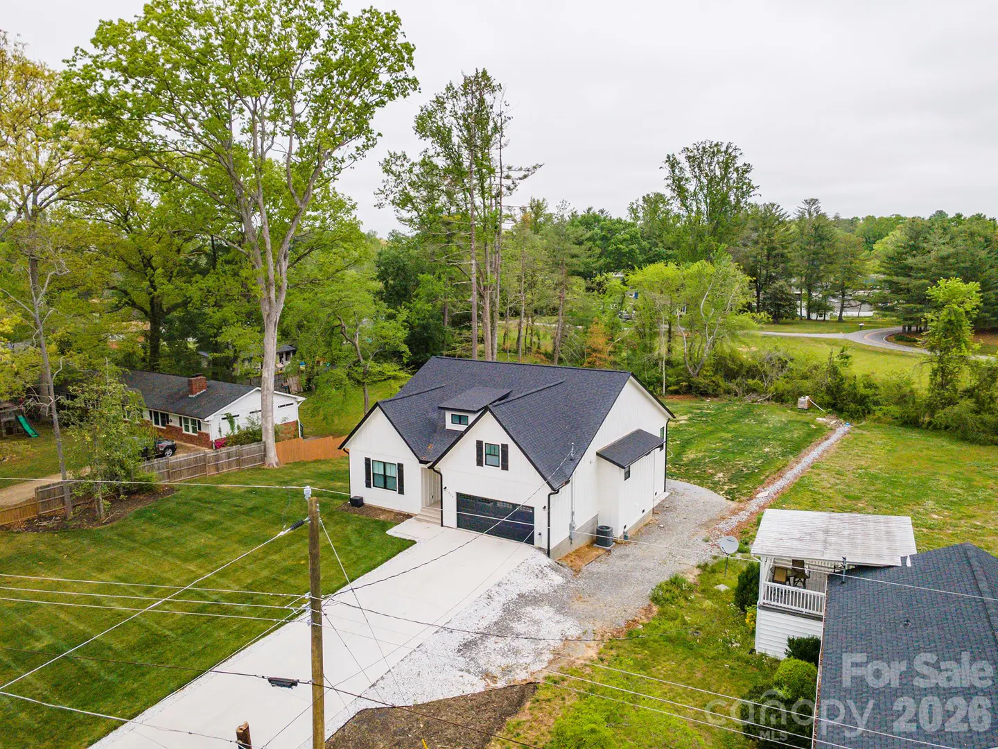 Aerial view of a modern white house with a black roof and a long driveway, surrounded by green trees and lawns.