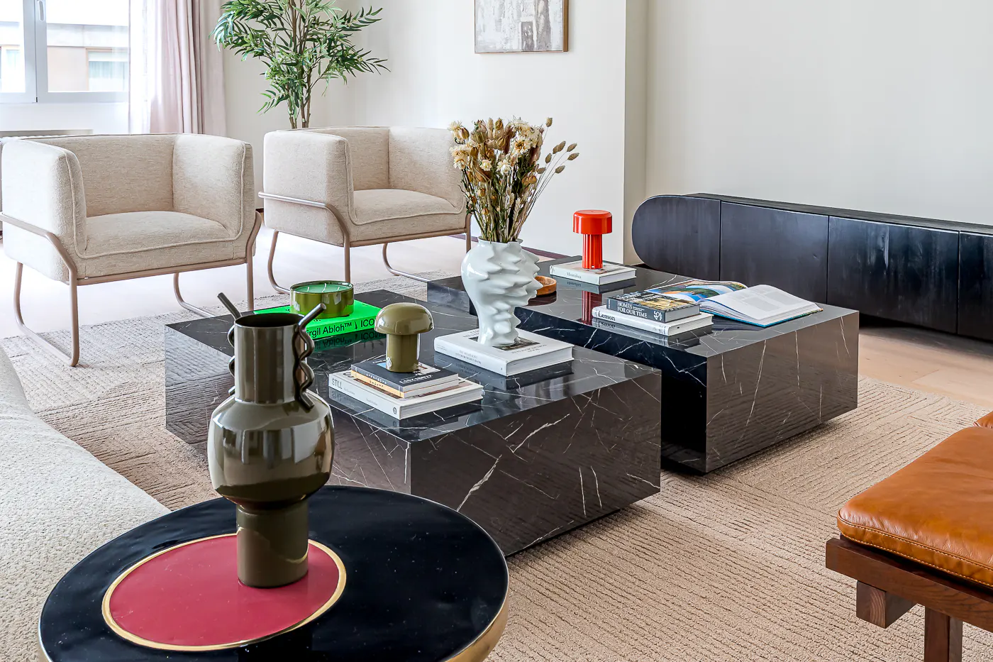 Living room with two beige armchairs, black marble coffee tables, and decorative vases and books.