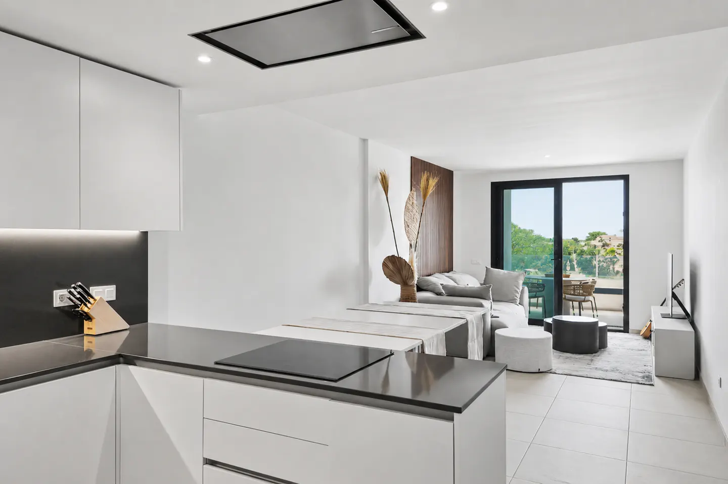 Bright, modern apartment interior with white walls, gray countertops, and a living area with a sofa and balcony.