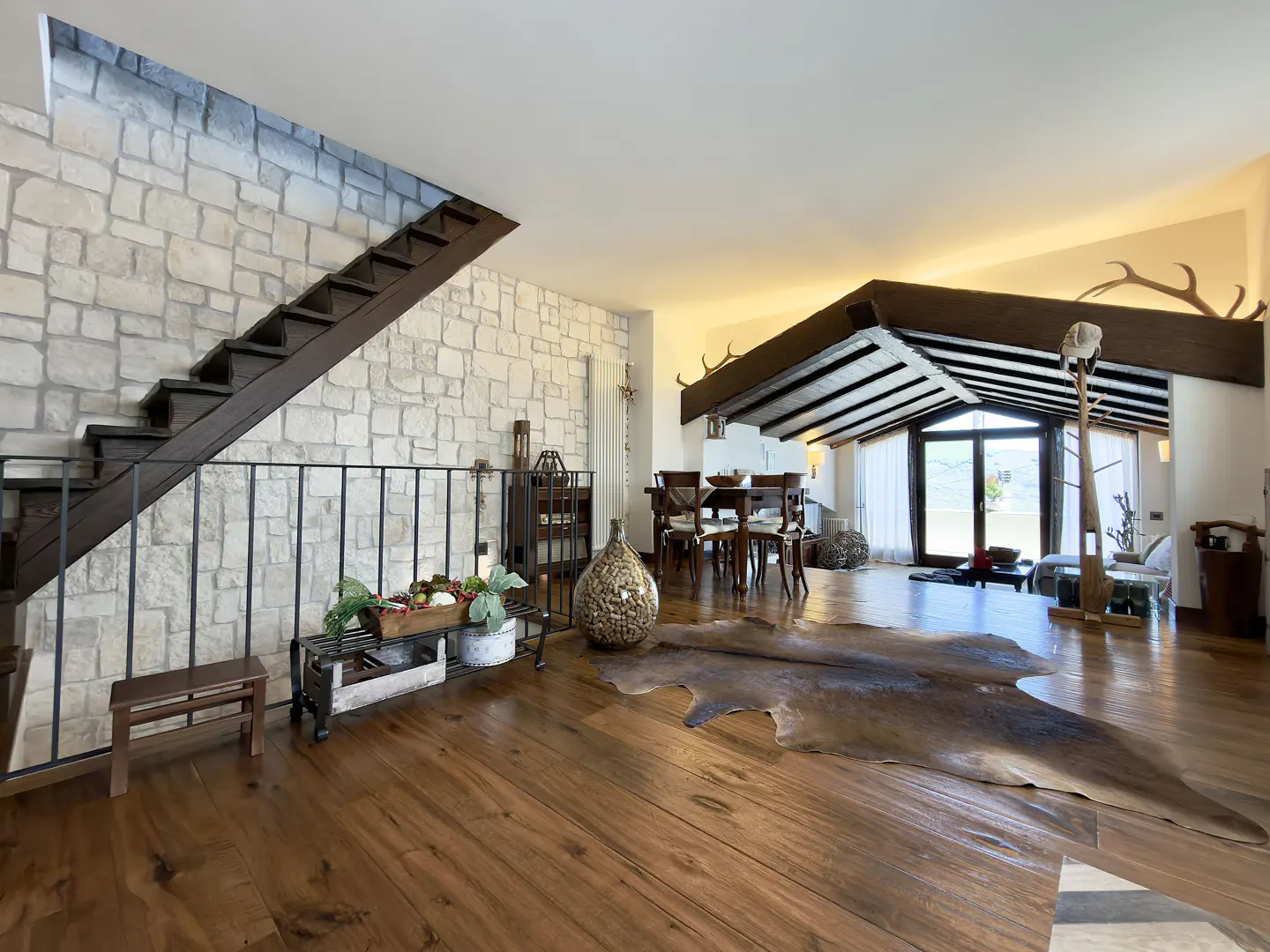 Open-concept living space with stone wall, dark wood stairs, and hardwood floors. A cowhide rug sits in the center of the room.