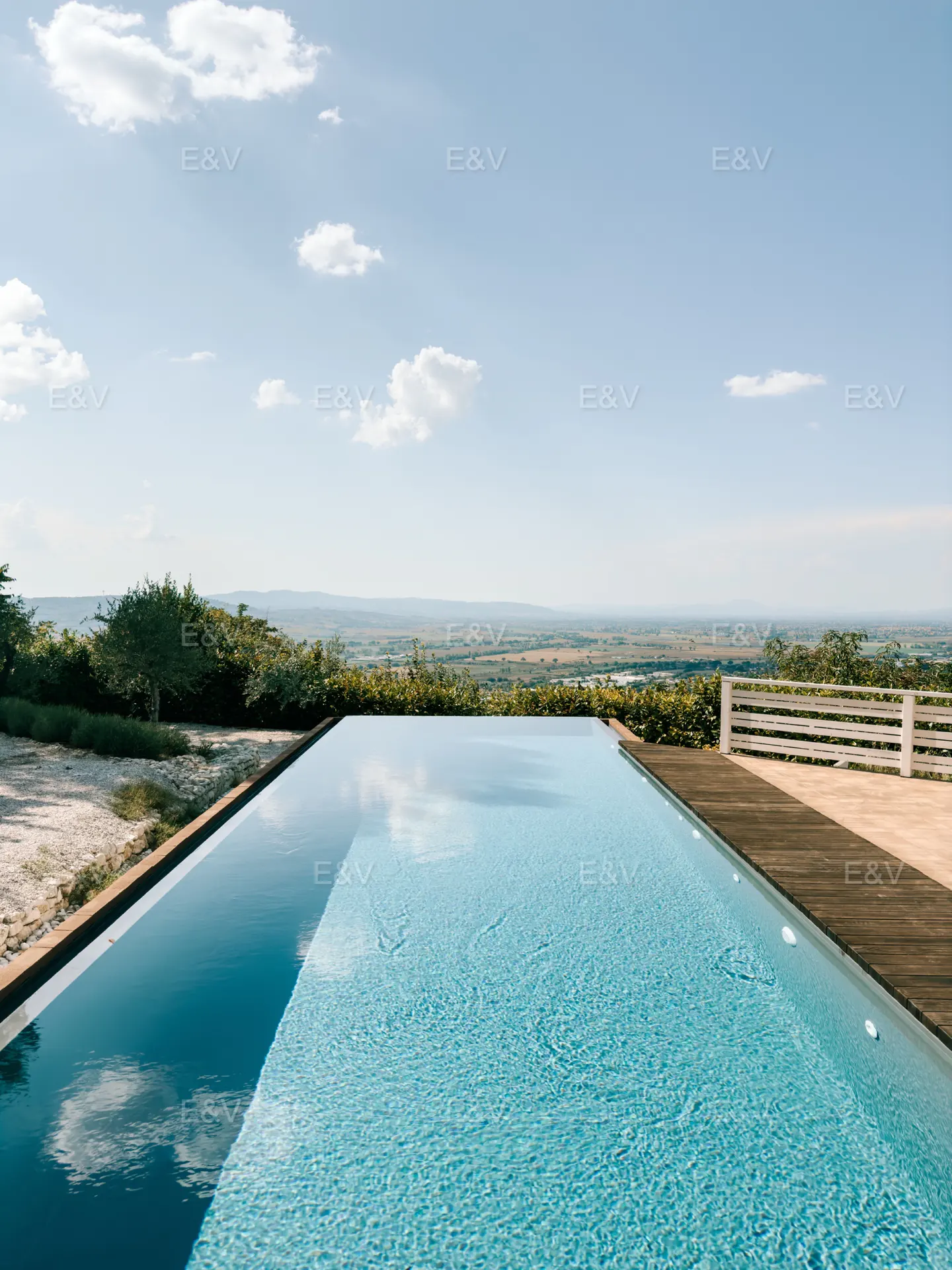 Infinity pool with blue water overlooking a green landscape under a blue sky with white clouds.