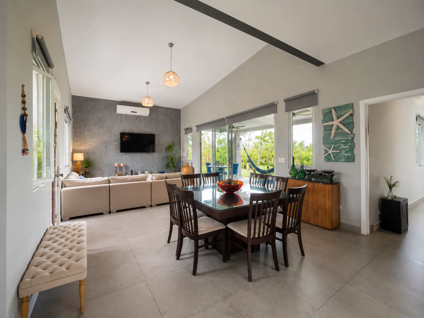 Open-concept living and dining area with a square table, beige sofa, and outdoor view.