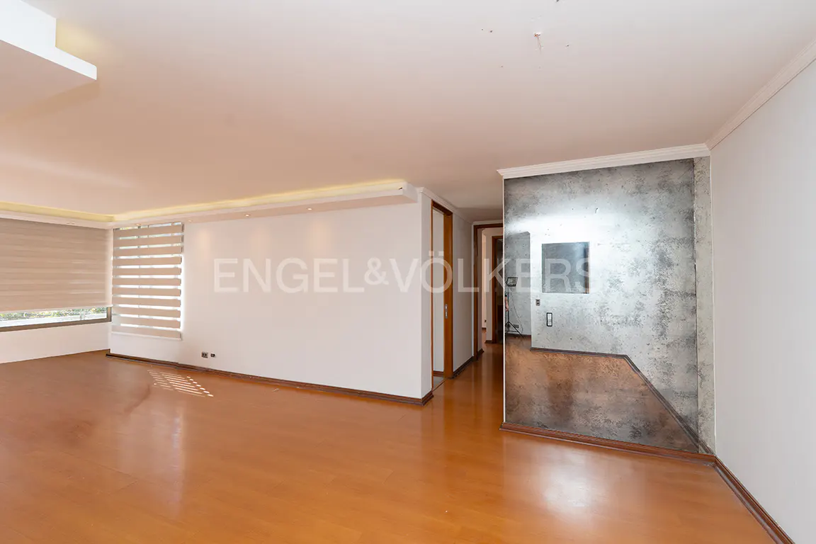An empty living room with wood floors, white walls, and a gray accent wall. Blinds cover a window.