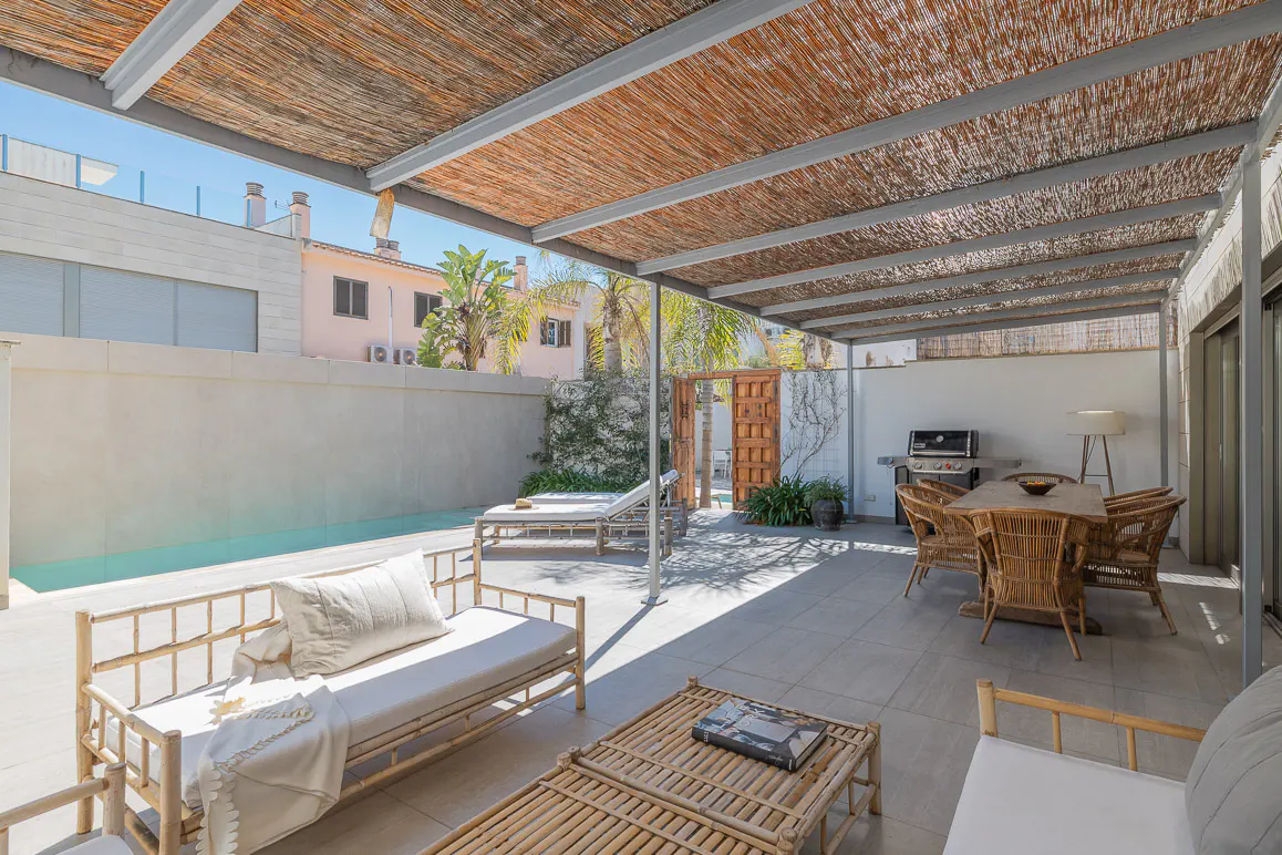 Outdoor patio with a bamboo pergola, lounge seating, and dining area. A pool is visible on the left.