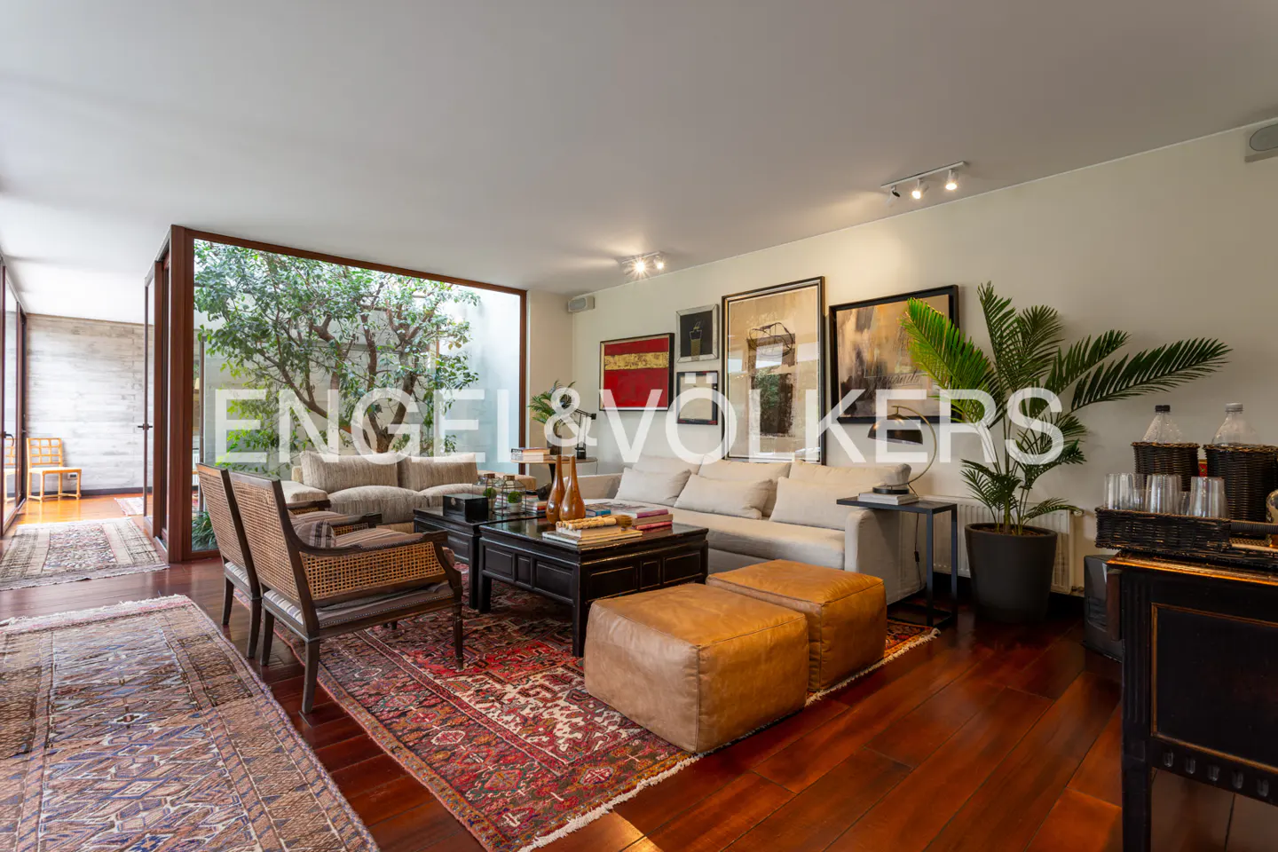 Spacious living room with hardwood floors, white sofa, black coffee table, and a large window overlooking a garden.