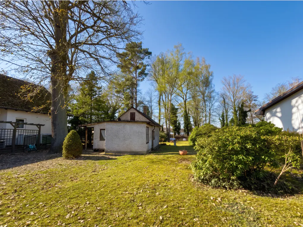 Exterior view of a small, white house with a green lawn and trees under a blue sky.